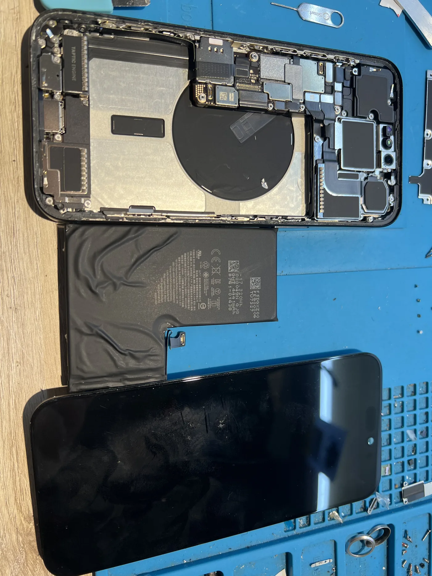 iPhone 15 Pro 拆機,中間是取出的變形舊電池,上方是機身內部,下方是分離的螢幕