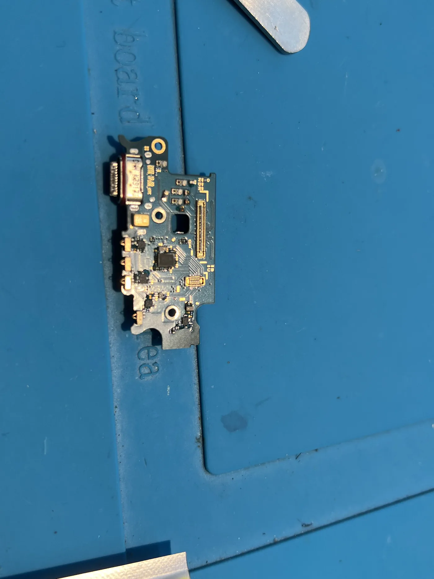 三星 Galaxy S22+ 拆下的尾插小板放在藍色維修墊上