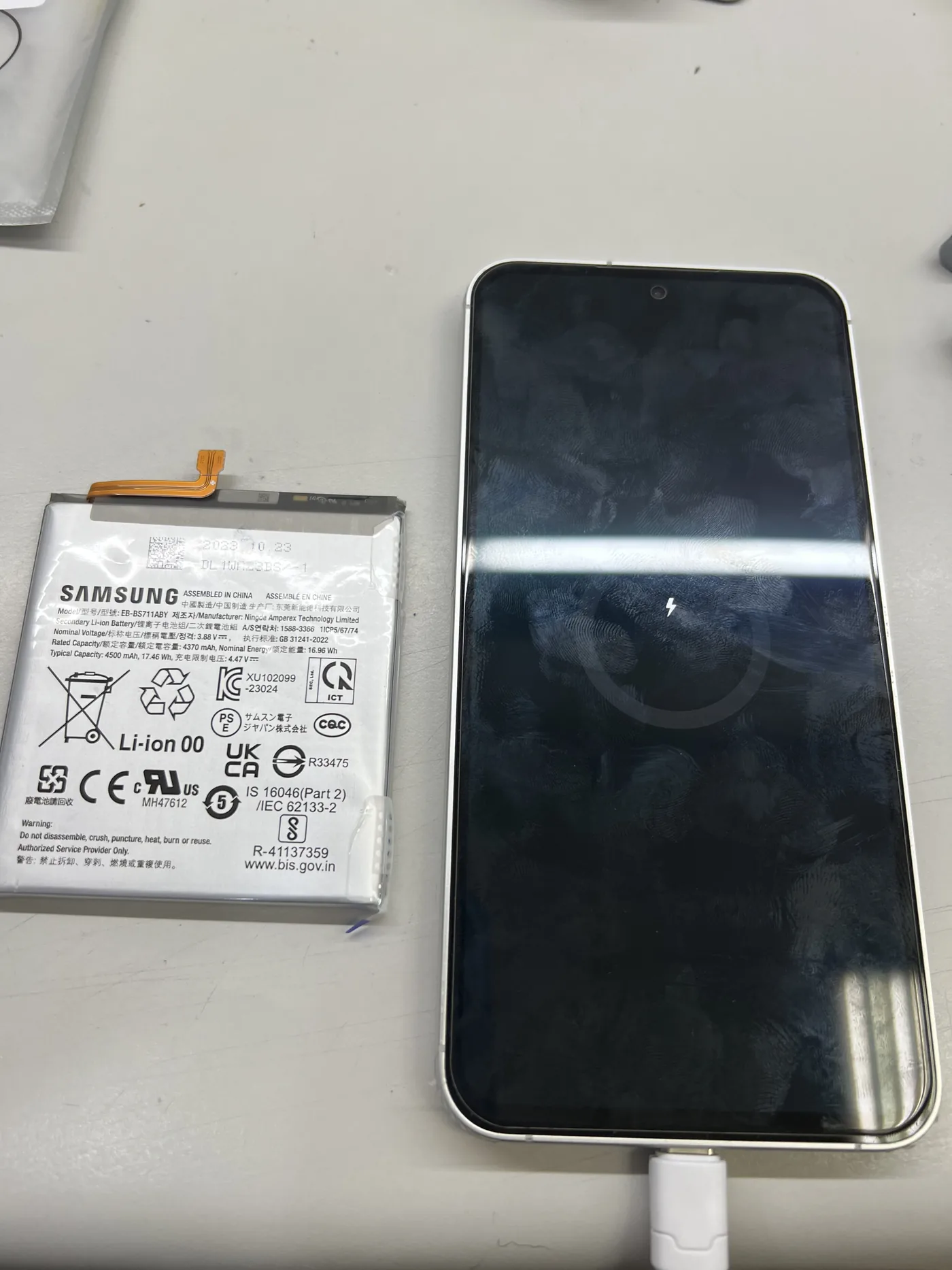 三星 Galaxy S23 FE 左邊是換下的舊電池,右邊接上充電線顯示充電中